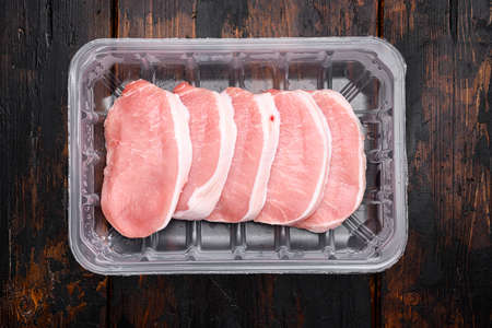 Uncooked pork chop set, in plastic pack container, on old dark wooden table background, top view flat layの写真素材