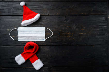 Funny santa from medical mask, red cap set on black wooden table background, top view flat lay with copy space for textの写真素材
