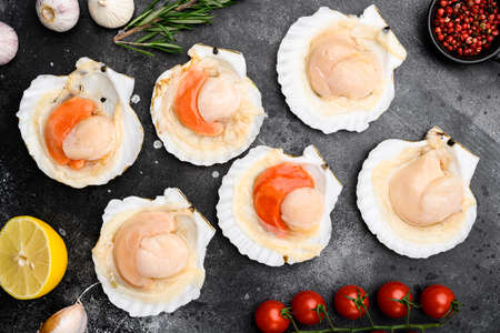 Seafood. Shellfish. Raw scallops with lemon set, on black dark stone table background, top view flat layの写真素材