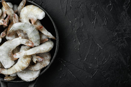 Frozen raw uncooked tiger prawns, shrimps set, in cast iron frying pan, on black stone background, top view flat lay, with copy space for textの写真素材