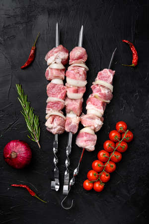 Kebabs raw meat and vegetables on skewers set, top view flat lay, on black dark stone table backgroundの写真素材