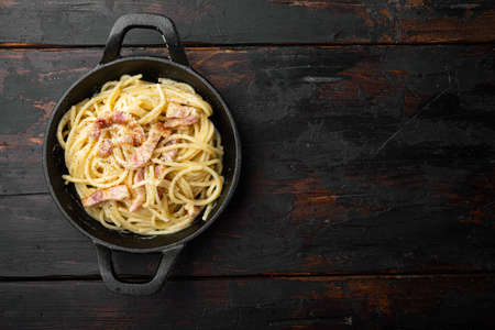Dish of Spaghetti Carbonara, modern italian recipe of pasta with guanciale, egg ad pecorino romano cheese set, in cast iron frying pan, on old dark wooden table, top view flat lay, with copy space for textの写真素材