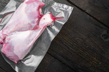 Raw turkey drumstick in vacuum plastic pack set, top view flat lay, with copy space for text, on black wooden table backgroundの写真素材