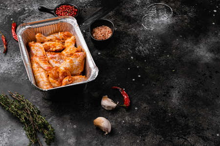 Fresh raw chicken wings and ingredients for bbq sauce set, on black dark stone table background, with copy space for textの写真素材