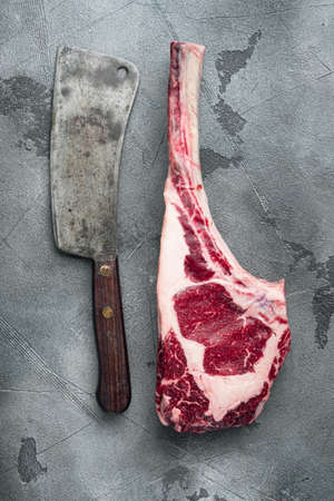 Raw tomahawk beef steak with ingredients for grilling with a spice rub set, and old butcher cleaver knife, on gray stone background, top view flat layの写真素材