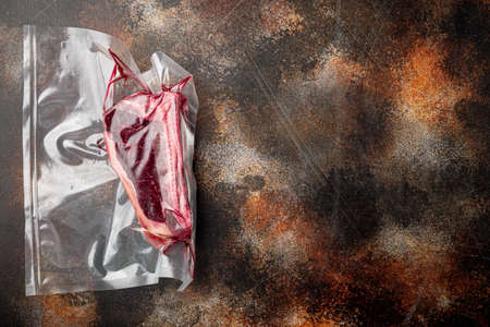 Raw beef meat Club or striploin on the bone steak in plastic airtight pack set, on old dark rustic background, top view flat lay, with copy space for textの写真素材