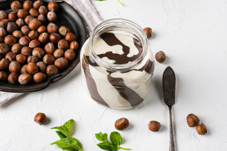 Chocolate spread or nougat cream with hazelnut set, on white stone table background, with copy space...