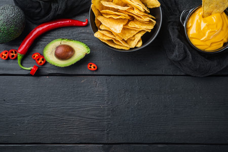 Triangular yellow corn tortilla chip with sauces, on black wooden background, top view or flat lay...