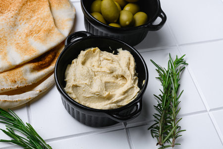 Bowl of tasty fresh hummus, on white ceramic squared tile table backgroundの写真素材