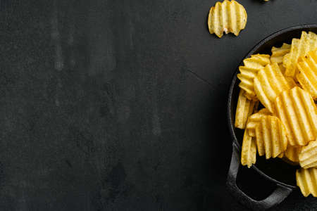 Ridged potato chips, on black dark stone table background, top view flat lay, with copy space for textの写真素材
