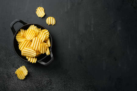 Wavy Salt Pepper Flavored Potato Chips, on black dark stone table background, top view flat lay, with copy space for textの写真素材