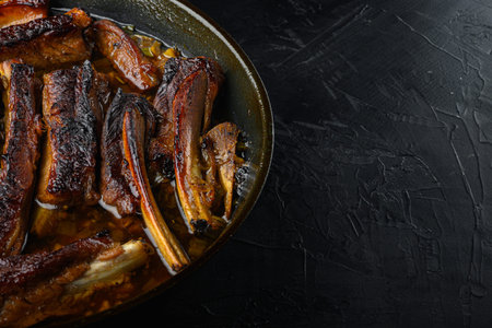 Pork ribs grilled with BBQ sauce and caramelized in honey set, in frying cast iron pan, on black...