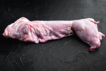 Whole raw rabbit meat set, on black stone background, with copy space for text