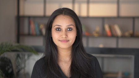 Beautiful smiling confident young Indian ethnic woman pretty face looking at camera posing alone at home in office, happy millennial Hindu ethnicity girl student professional close up front portrait.の写真素材