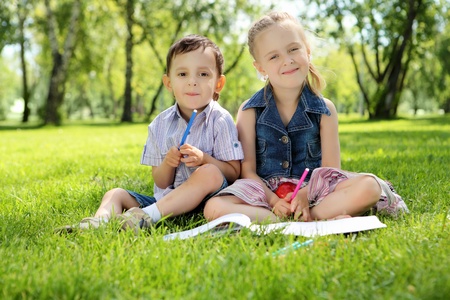 Sister and brother in the park reading a bookの写真素材