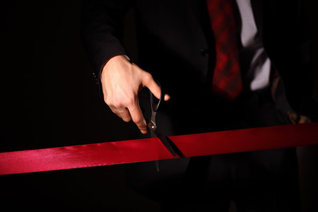 Hand of a businessman with scissors cuting a red ribbon