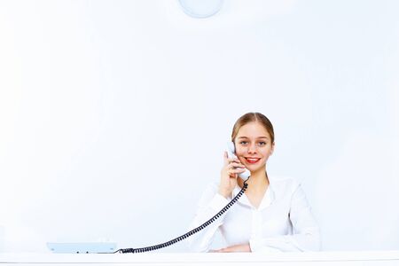 Young woman in business wear sitting with a phone in officeの写真素材