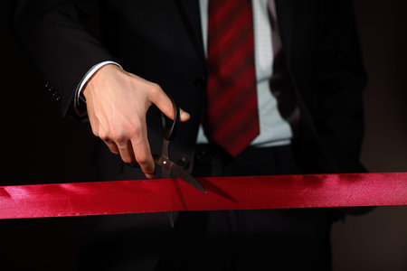Hand of a businessman with scissors cuting a red ribbon