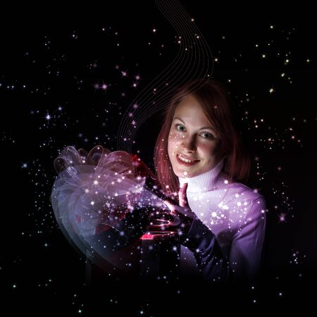 Young woman opening a gift box with shining and glittering lights around herの写真素材