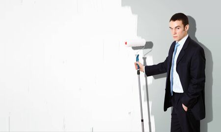 Young businessman with a paint brush against blank white wallの写真素材