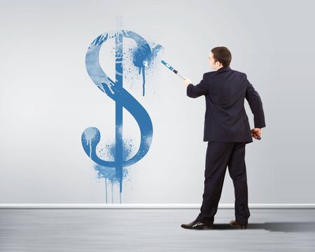 Young man with paint brush and banknote painted on the wallの写真素材