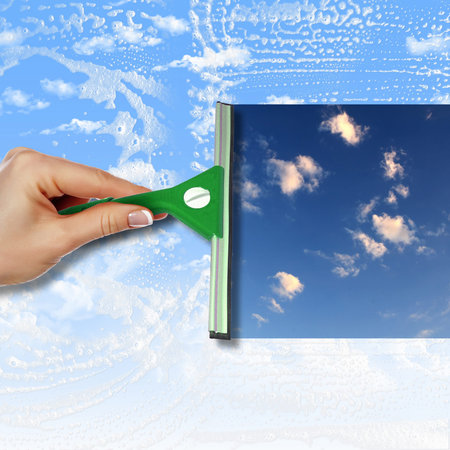 Hand cleaning window with blue sky and white clouds