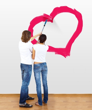 Young couple with paint brushes drawing heart on the wallの写真素材