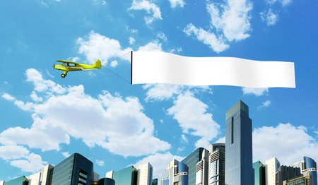 Plane in the sky above the city with blank flagの写真素材