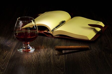 A glass with cognac, cigar and an old book nearbyの写真素材