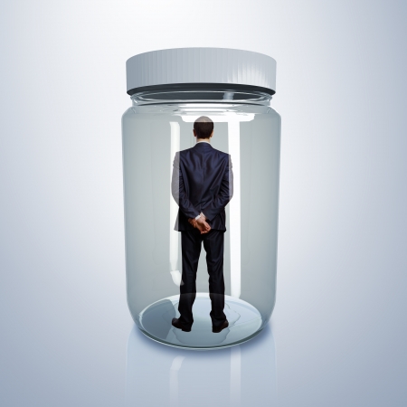 Businessman trapped inside a transparent glass jarの写真素材