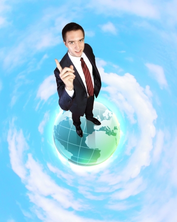 Planet earth against sky background and businessman standing on top of itの写真素材