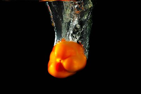 Colored orange paprika in water splashes on black backgroundの写真素材