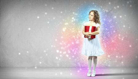 A cute young girl holding a christmas gift, dark background with christmas light bokehの写真素材
