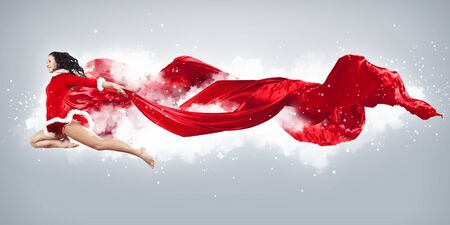 Happy smiling woman in red xmas costume jumping highの写真素材