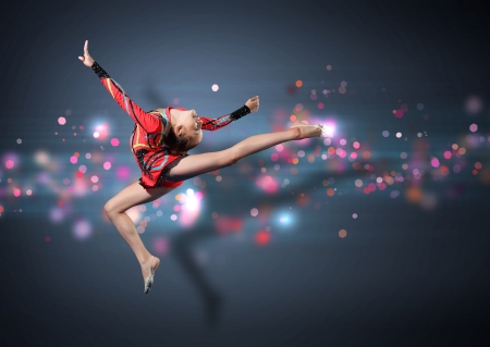 Young cute woman in gymnast suit show athletic skill on black backgroundの写真素材