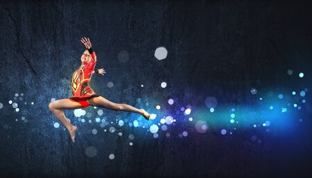 Young cute woman in gymnast suit show athletic skill on black backgroundの写真素材