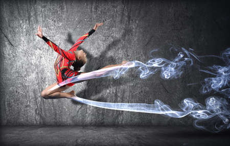 Young cute woman in gymnast suit show athletic skill on black backgroundの写真素材