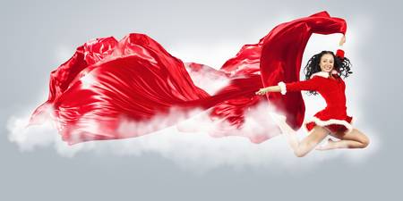 Happy smiling woman in red xmas costume jumping highの写真素材