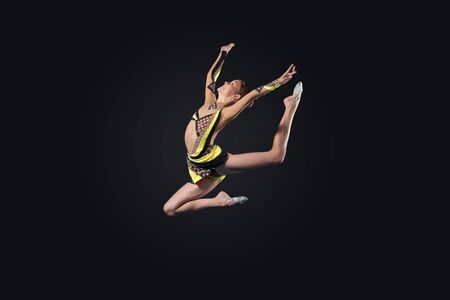 Young cute woman in gymnast suit show athletic skill on black backgroundの写真素材