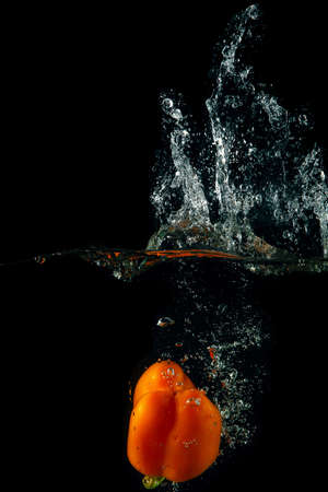 Colored orange paprika in water splashes on black backgroundの写真素材