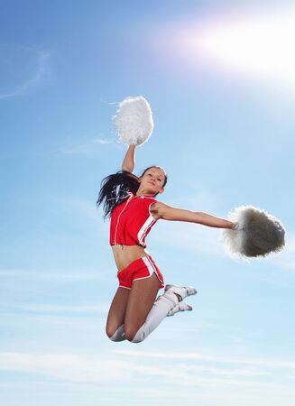 Young beautiful female cheerleader in uniform jumping highの写真素材