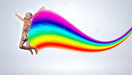 a little girl jumping and raising hands against rainbow backgroundの写真素材