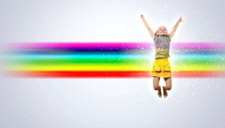 a little girl jumping and raising hands against rainbow backgroundの写真素材