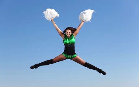Young cheerleader in green costume jumping against blue skyの写真素材