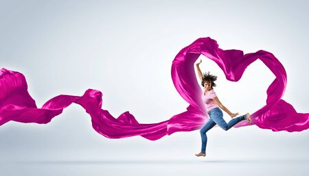 Young woman dancing with red fabric in studio and heart symbolの写真素材