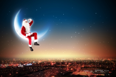 Santa Claus on the moon above a city at nightの写真素材