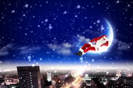 Santa Claus on the moon above a city at nightの写真素材