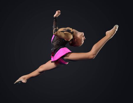 Young cute woman in gymnast suit show athletic skill on black backgroundの写真素材