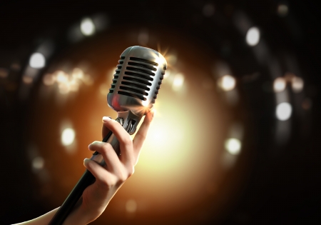 Female hand holding a single retro microphone against colourful backgroundの写真素材