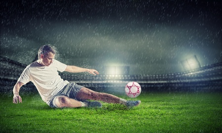 football player in white shirt striking the ball at the stadium under the rainの写真素材